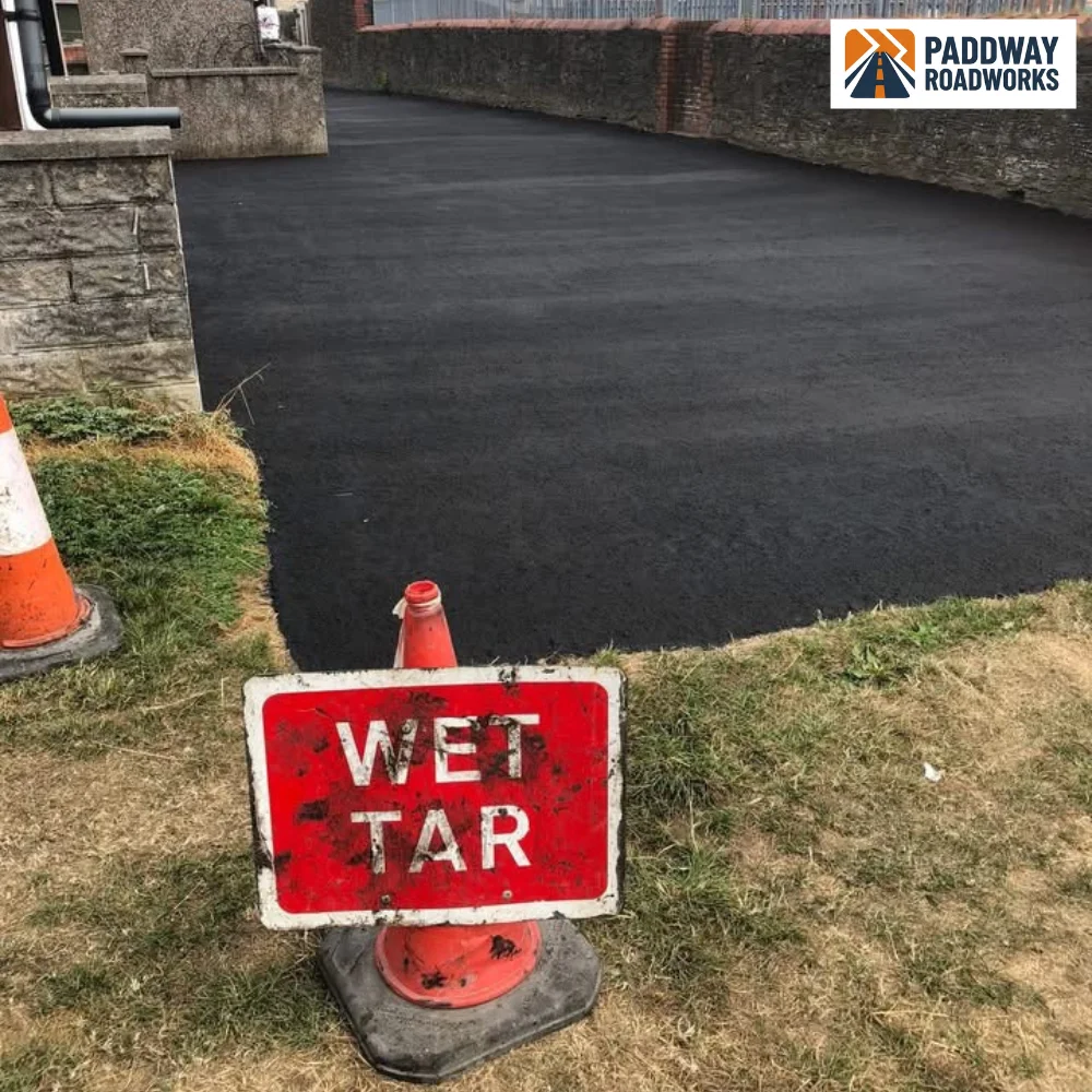 Tarmac driveway finished with traffic cones and hi-vis "WET TAR" sign in foreground.