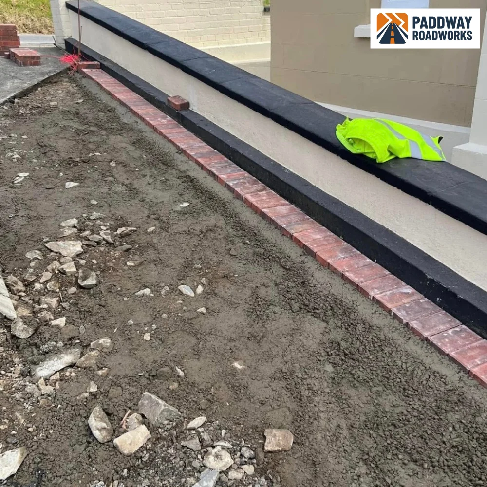 Block paving install in progress against rendered house wall.