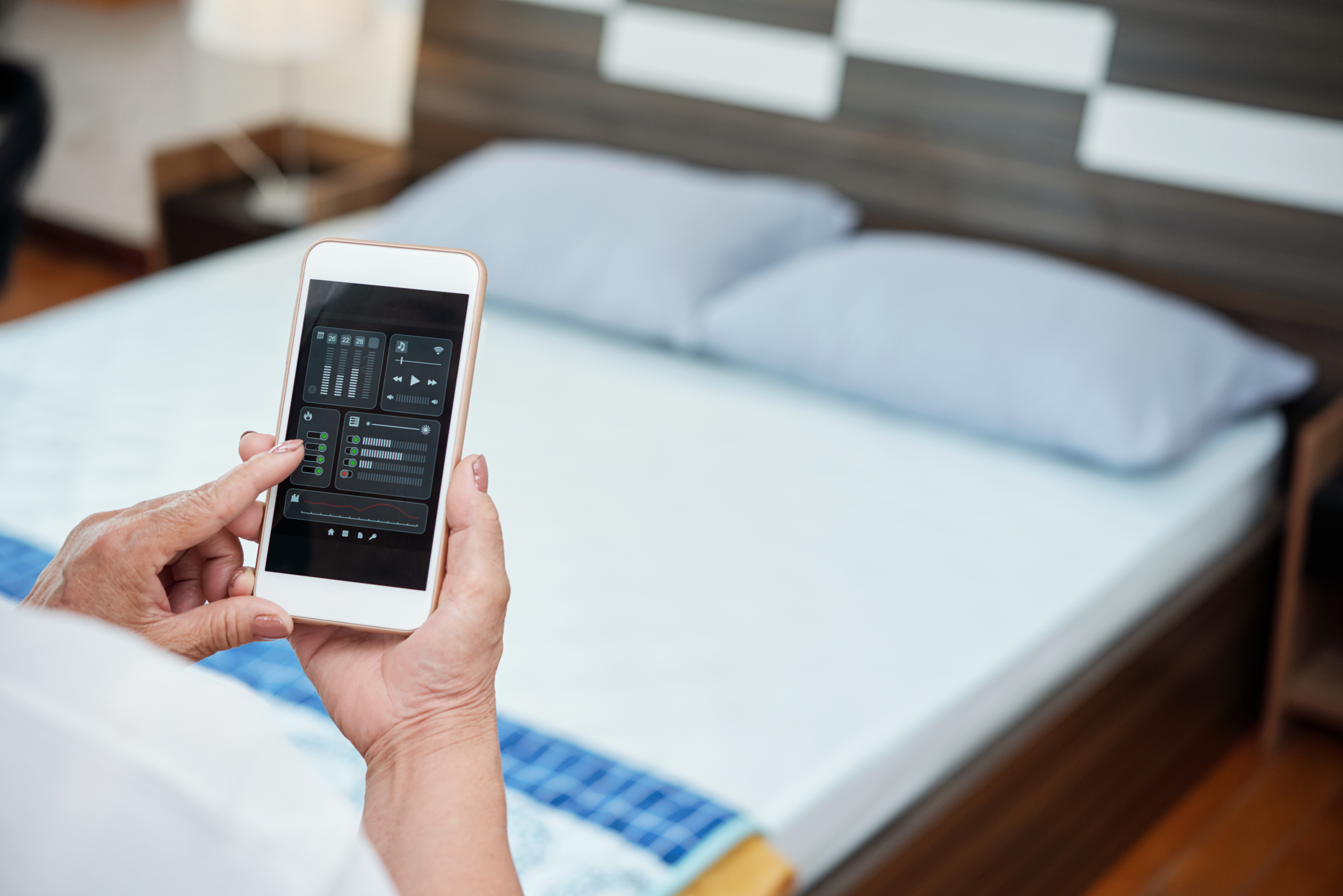 Woman adjusting an active cooling mattress from her phone while seated on the bed