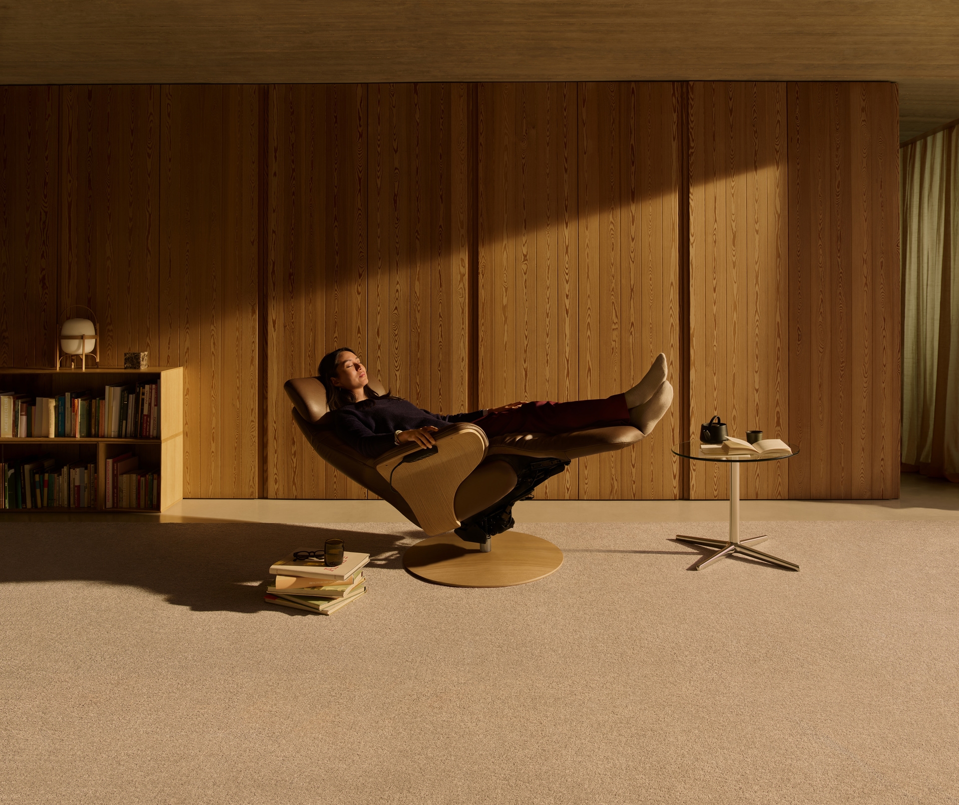 A woman reclining fully in a Stressless recliner, feet up, in a sunlit wood panelled room