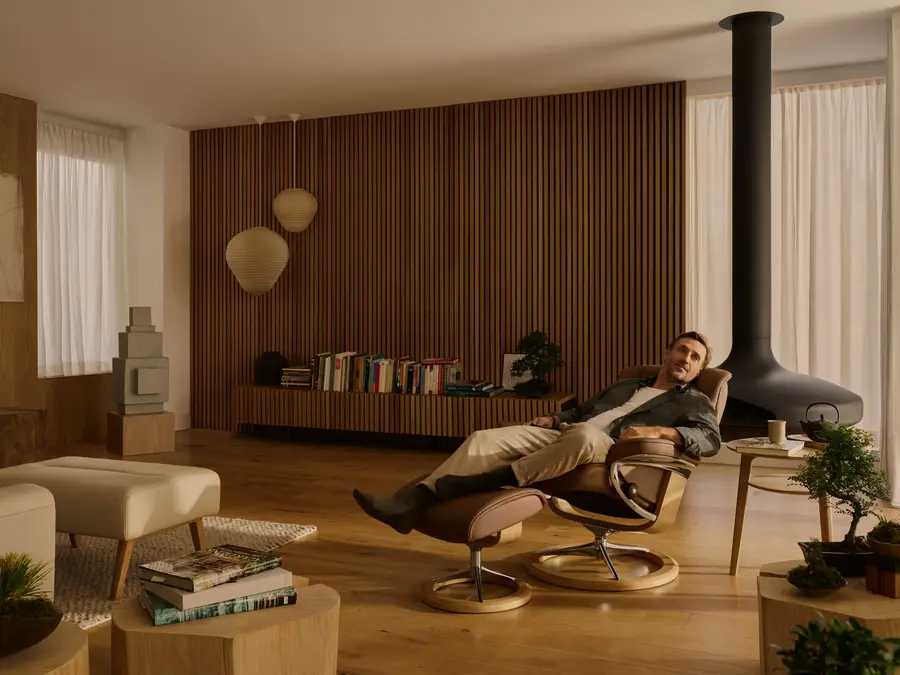 A man reclining in a Stressless recliner with the ottoman, in a warm wood panelled living room