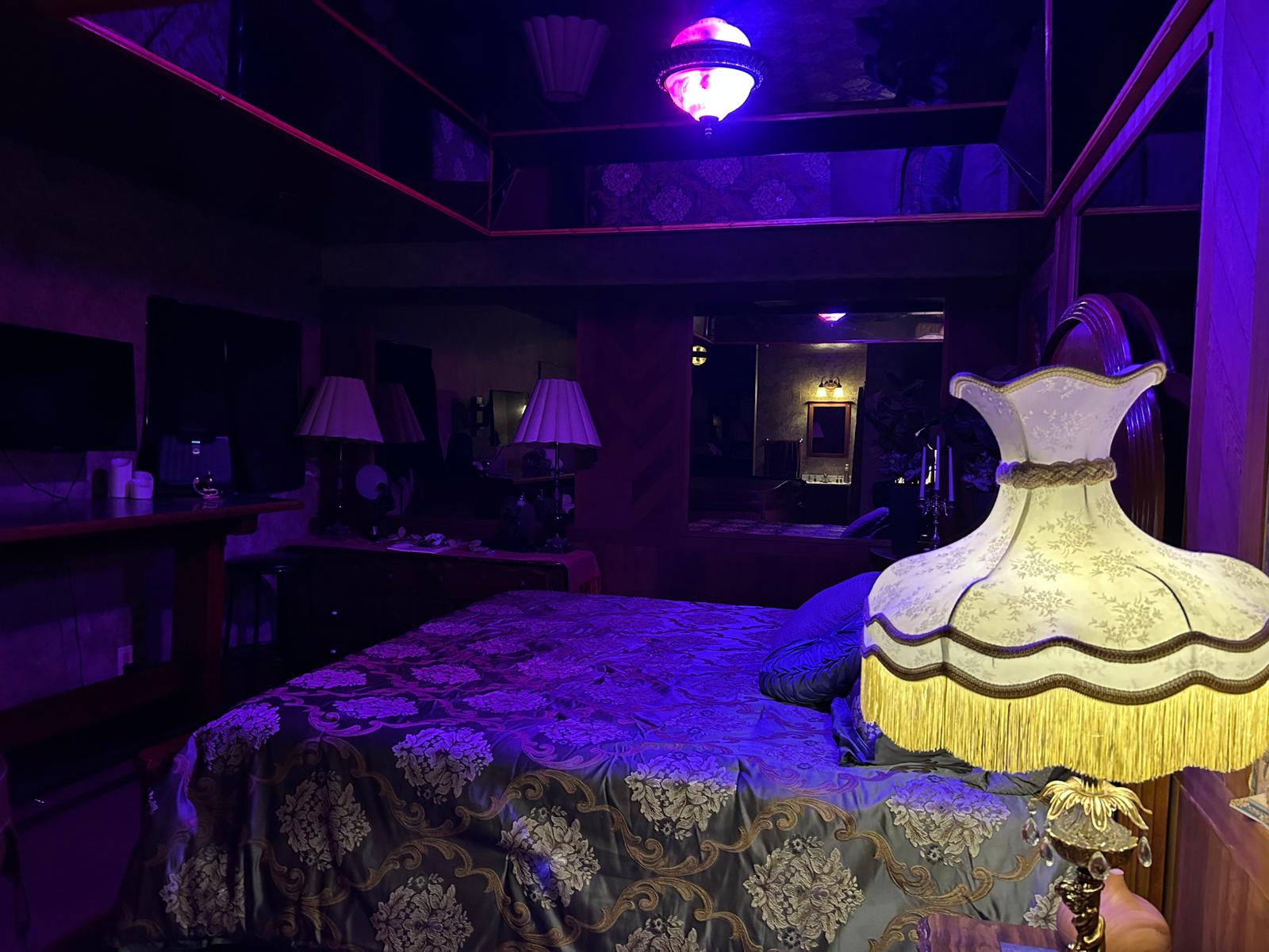 Luxuriously decorated private room with patterned bedding, ornate lamps, mirrors, and atmospheric purple lighting