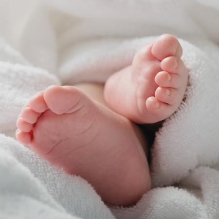 Nackte Babyfüßchen schauen aus einer weichen, weißen Decke heraus 