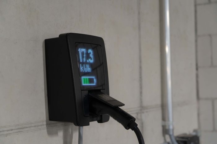 Cargador de pared con pantalla, conectado al coche, junto a un tubo de canalización en un garaje