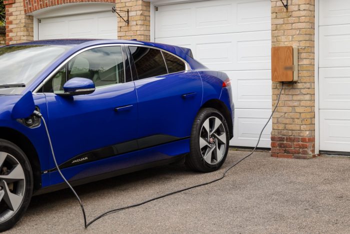 Coche eléctrico azul cargando frente a la puerta del garaje de una vivienda