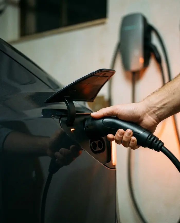 Mano conectando el conector de carga a un coche eléctrico en un garaje de noche