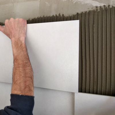 Installing large white tiles on a wall with fresh mortar