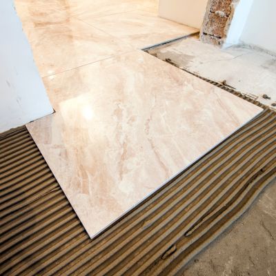 Marble-look floor tile being installed over a mortar base