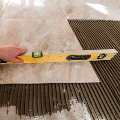 Contractor using a level tool to ensure precision in laying large marble-look floor tiles