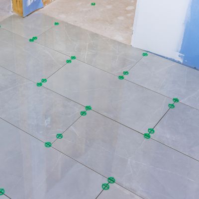 Gray marble floor tiles being precisely aligned with green tile spacers