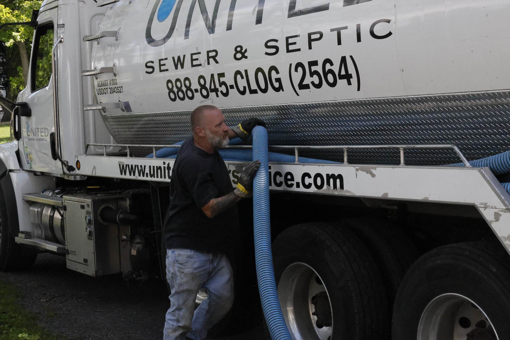 United Sewer and Septic technician handling a vacuum hose beside the service truck