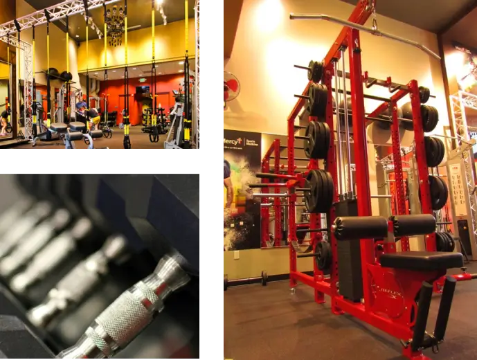 A gym with various exercise equipment includes a red machine with weight stacks, a rack of dumbbells, and suspension trainers hanging from the ceiling.