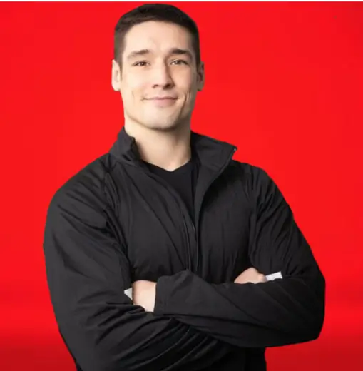 Lucas Leggette, a certified personal trainer with short dark hair and wearing a black jacket, stands with arms crossed against the vibrant red backdrop of Red Fitness Lounge.