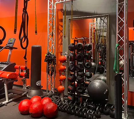 A gym interior with red and black decor, various weightlifting equipment, and three artwork pieces of light bulbs on the wall above.