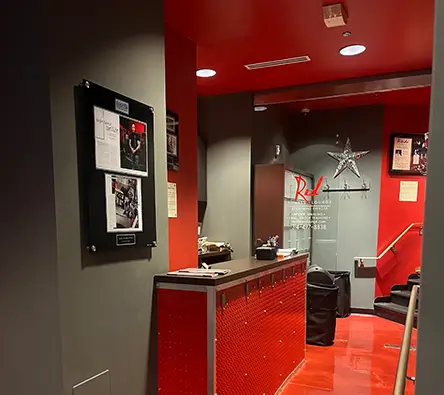 A hallway with red walls and flooring leads to a reception desk. The wall has framed pictures and documents. A star decorates the back wall near stairs.