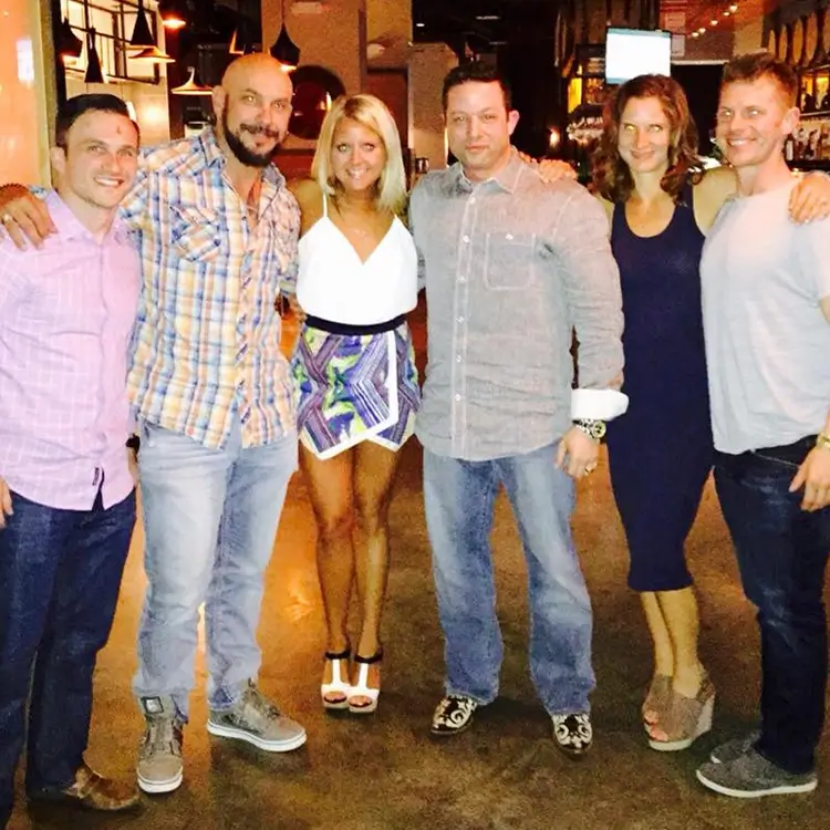 Six people standing together smiling in a restaurant or bar setting.