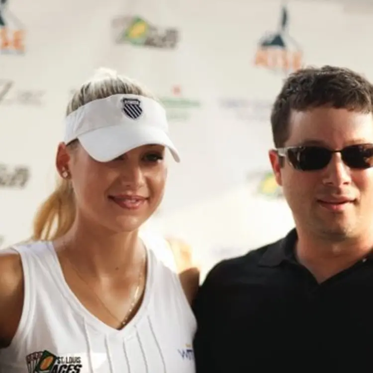 Two people posing for a photo; the person on the left wears a white visor and sports attire, while the person on the right wears dark sunglasses and a black shirt.