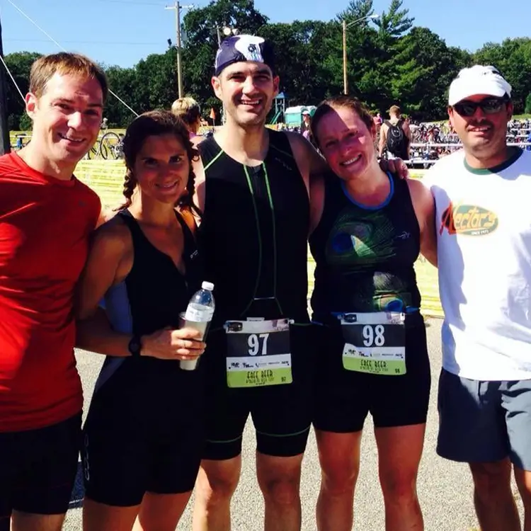 Five people, wearing athletic gear and race bibs, stand together and smile for a group photo outdoors.