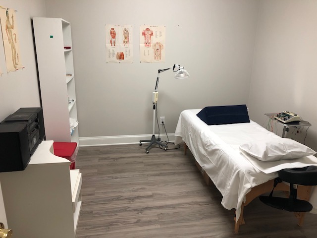Treatment room at Shanghai Acupuncture Clinic - fresh linens, heat lamp, electro-stimulation unit, anatomy and meridian posters on the wall