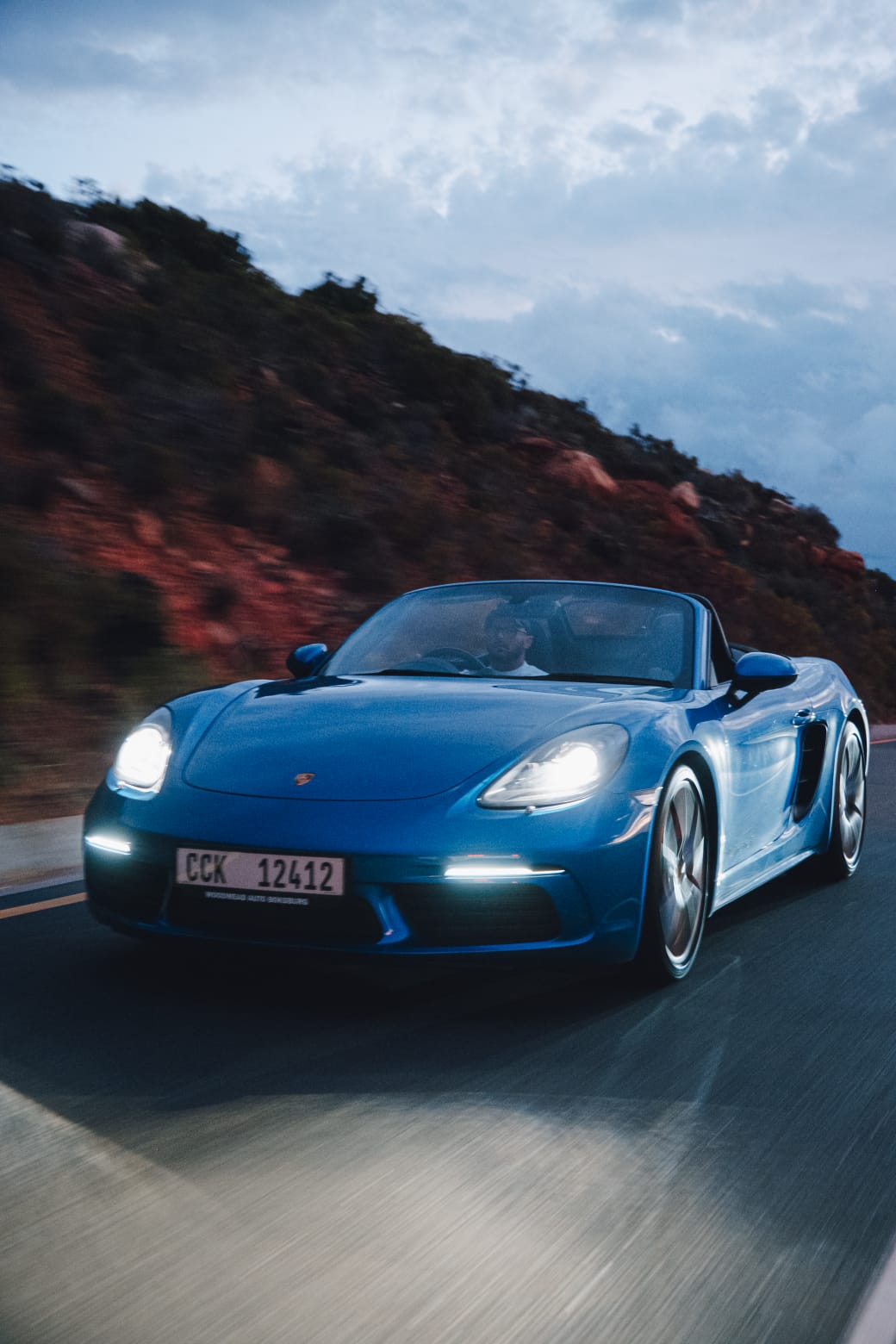 Blue 2017 Porsche Boxster 718 S driving on the road with the roof down.