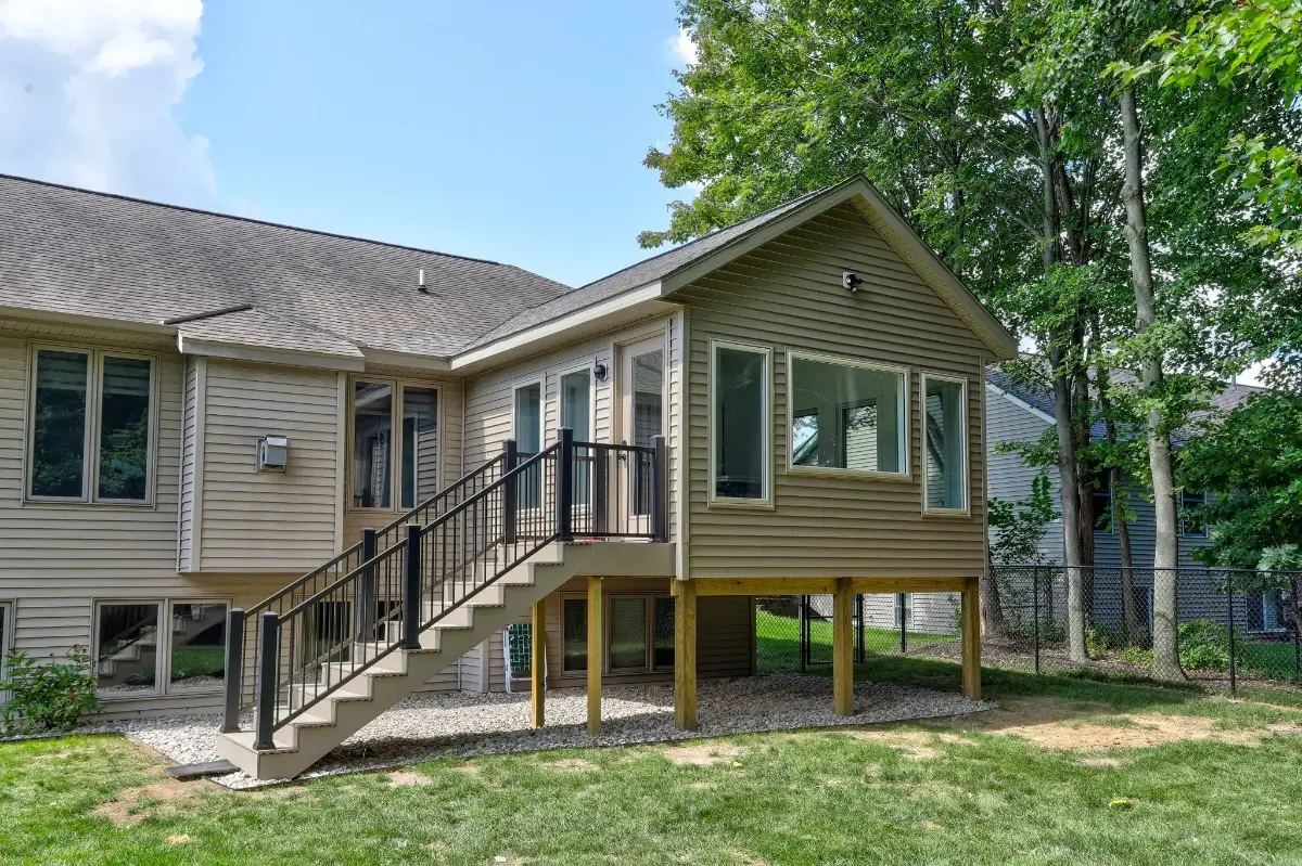 Two-story home addition in Grand Rapids, Michigan with matching olive siding, new windows and a railed entry stair