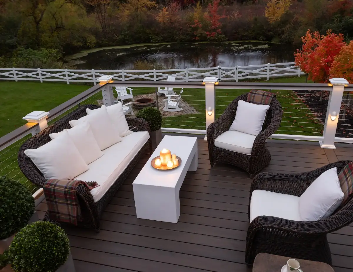 Composite deck in Grand Rapids, Michigan with a white pergola, outdoor sectional and a fire table overlooking a pond