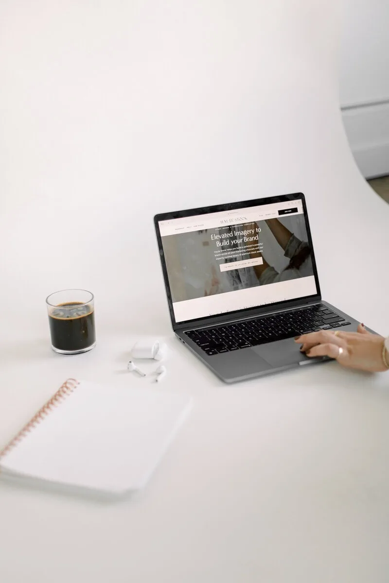 Laptop on a white desk beside coffee, a notebook, and earbuds. Laptop on a white desk beside coffee, a notebook, and earbuds.