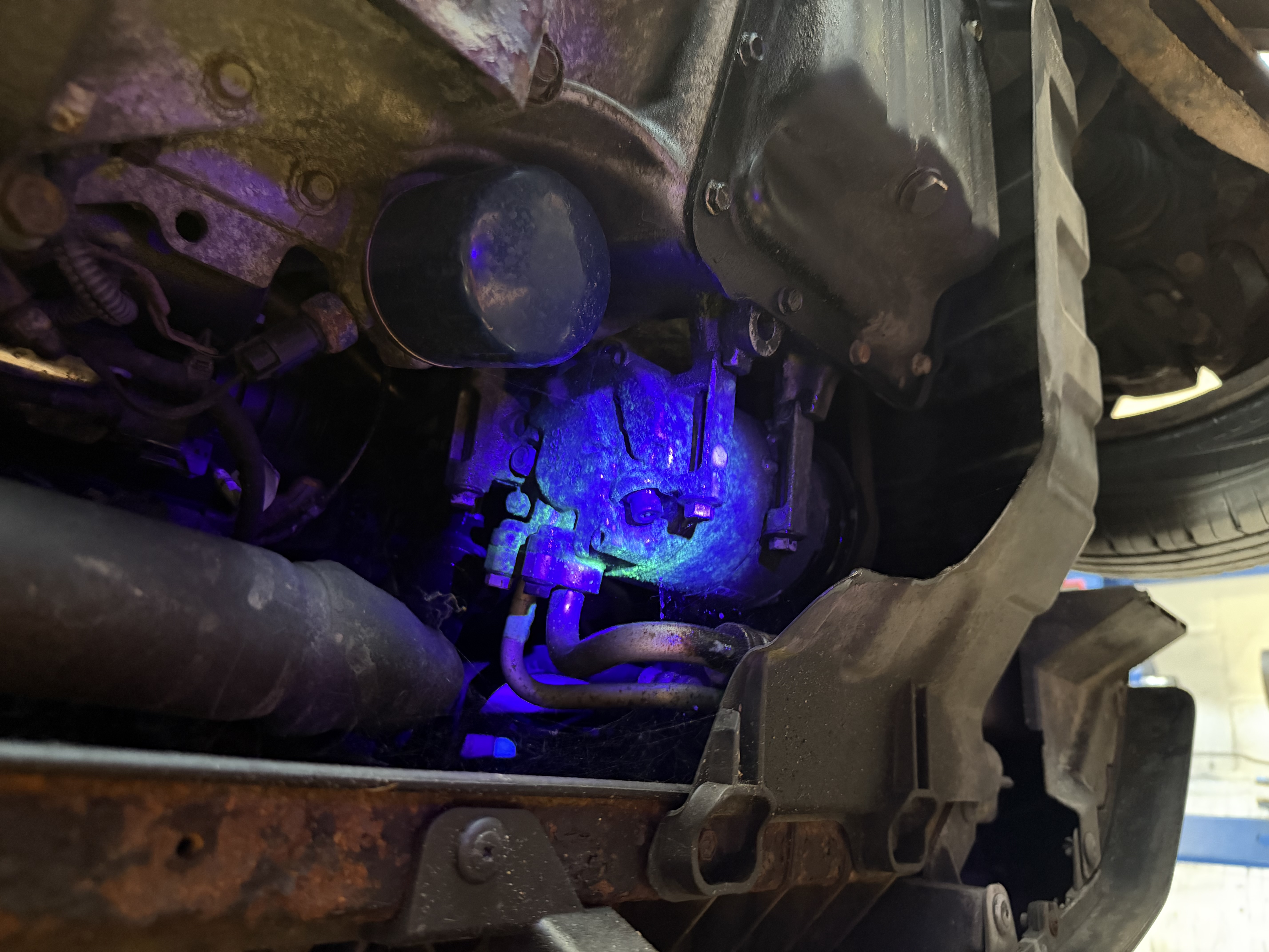 Underside of a vehicle inspected under UV light for leak detection at Shaw's Service Station