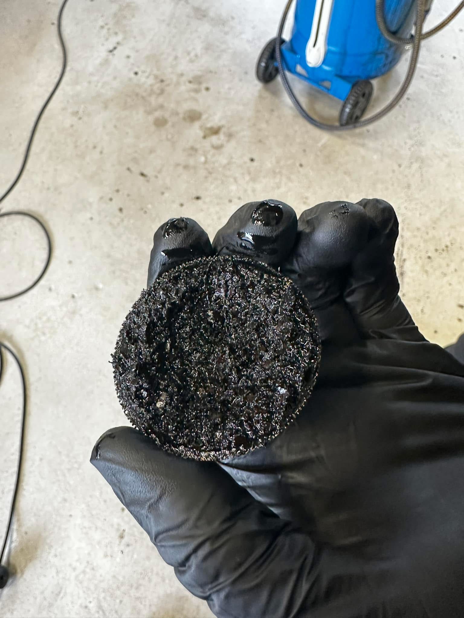 Ford 1.0 EcoBoost oil pickup strainer removed and held in gloved hand, heavily contaminated with black sludge, at Shaw's Service Station Rhyl