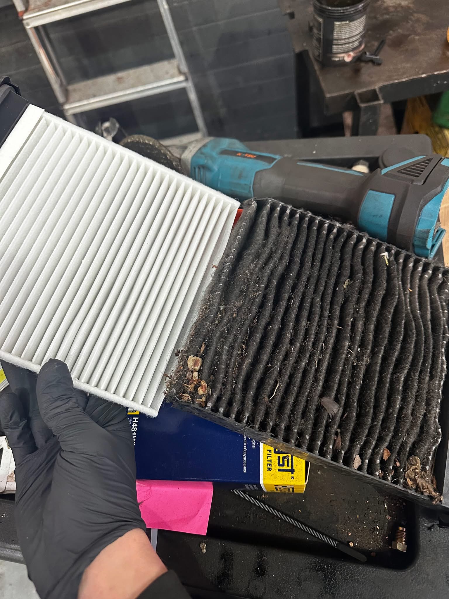 Old dirty cabin air filter compared to a new clean replacement, held side by side in a gloved hand at Shaw's Service Station