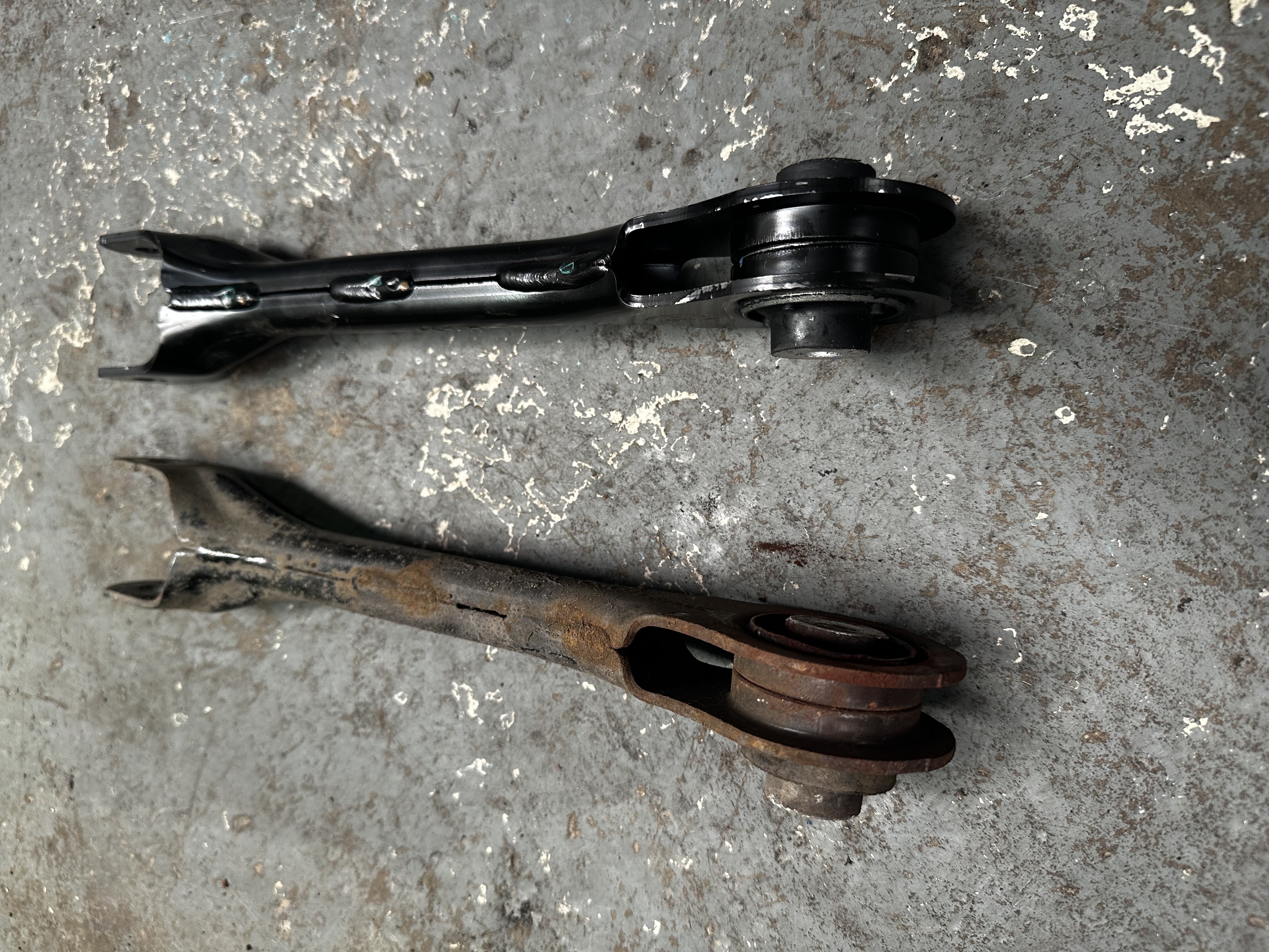 Old cracked and rusted control arm alongside its new replacement at Shaw's Service Station