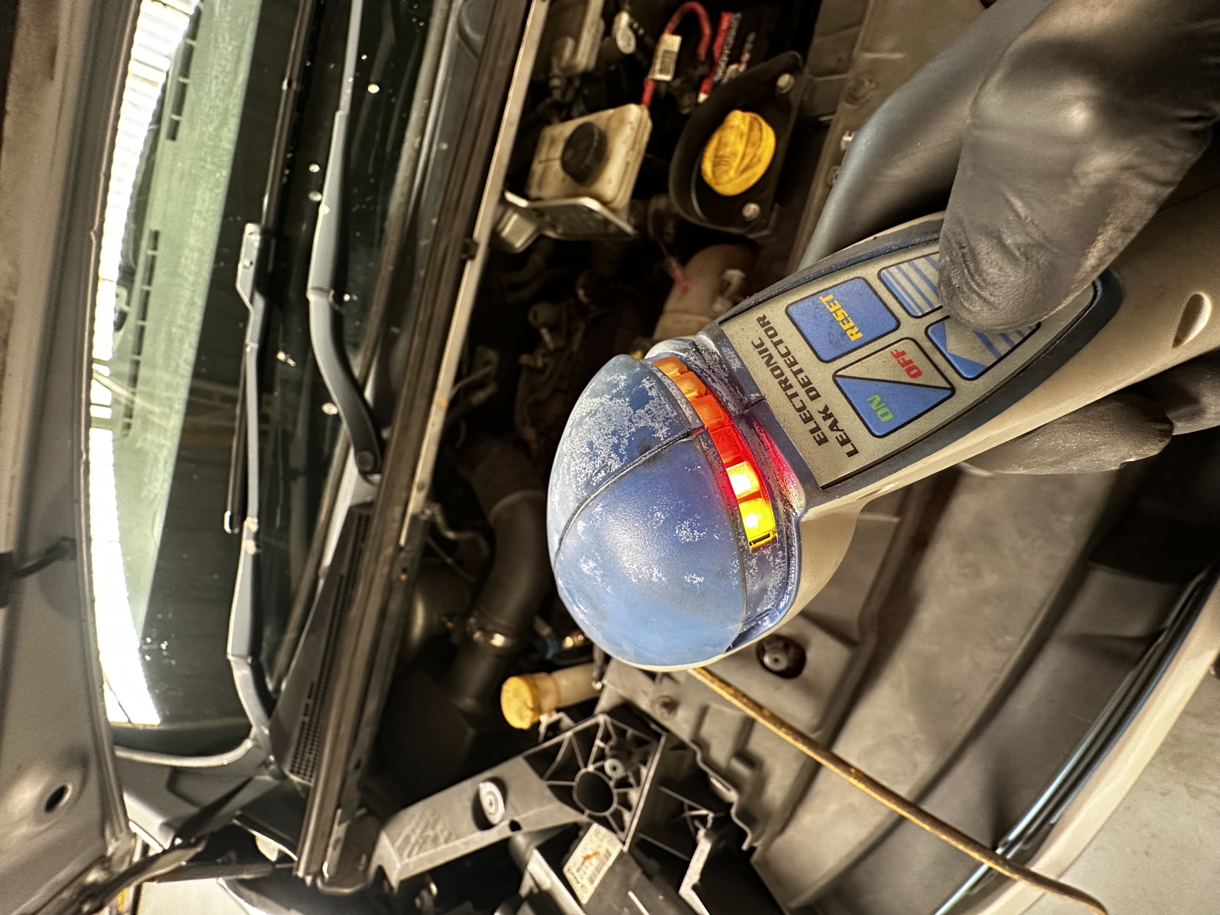 Electronic leak detector being used to check for refrigerant leaks in a vehicle engine bay at Shaw's Service Station