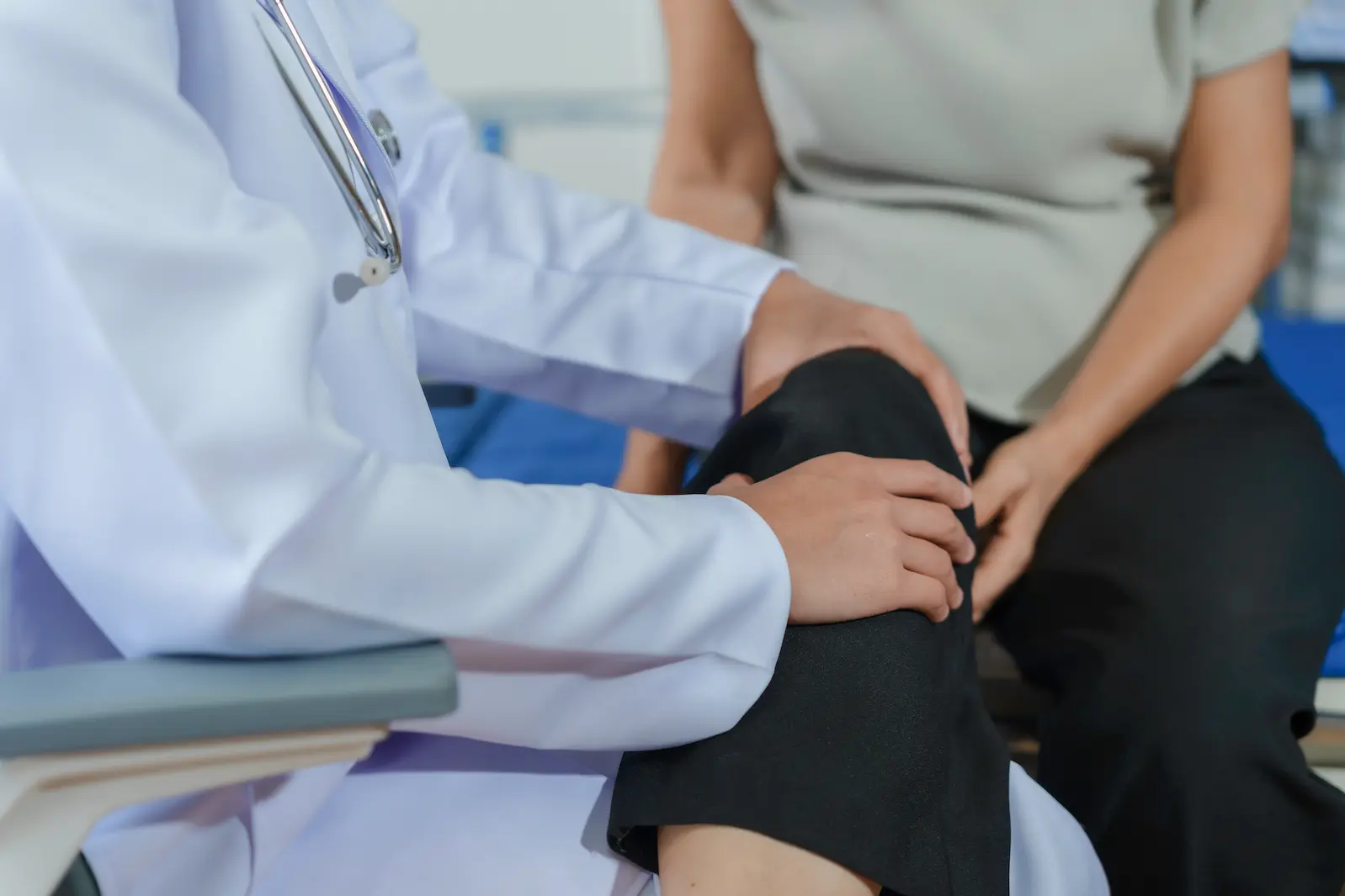 Close-up of a doctor in a white lab coat examining a patient's knee during a medical checkup.
