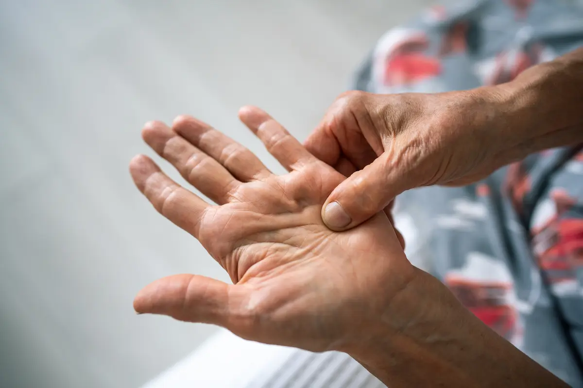 A close-up of a person's hands, with one thumb pressing firmly into the center of the other open palm, suggesting massage, and pain relief