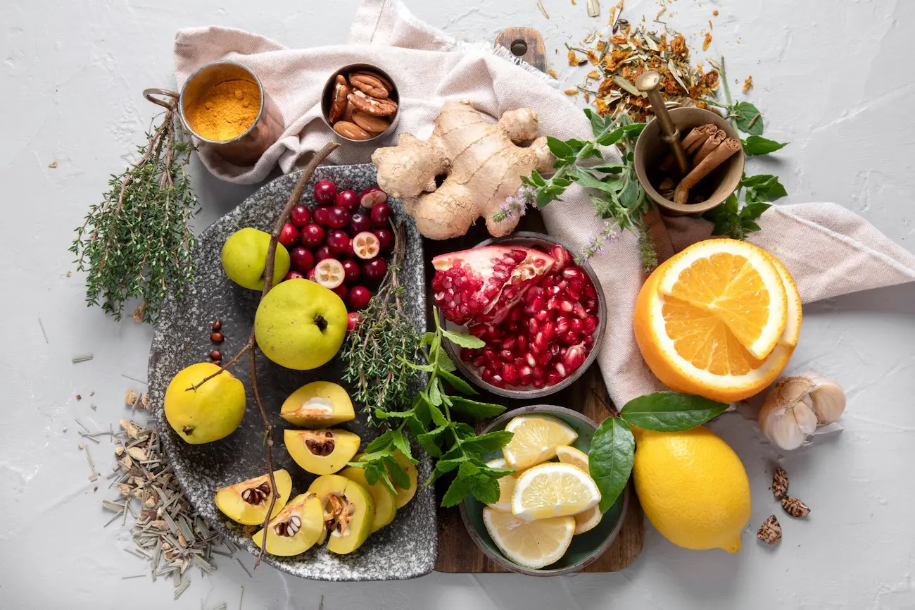 Top-view arrangement of fresh anti-inflammatory ingredients including pomegranates, ginger, citrus fruits, and fresh herbs.