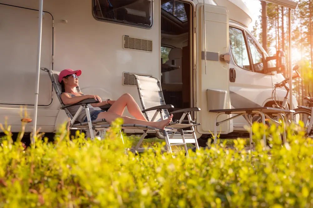 A woman relaxing on a lawn chair outside her parked camper van.