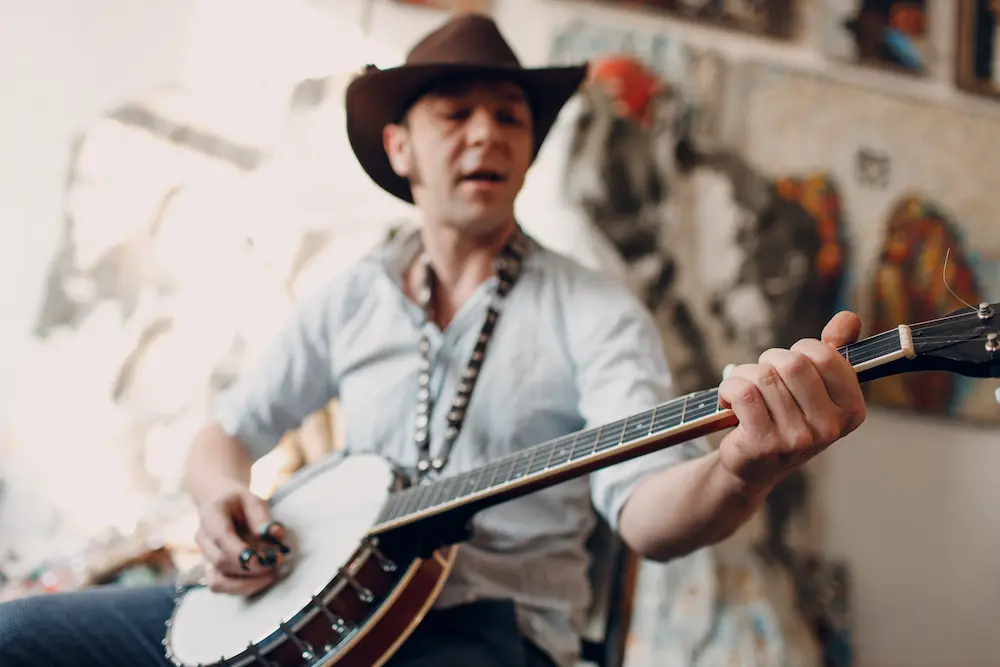 A man in a cowboy hat playing a banjo indoors.