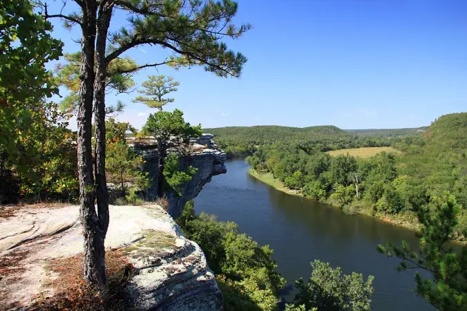 Scenic view of a river winding through lush green hills from a rocky cliff overlook.