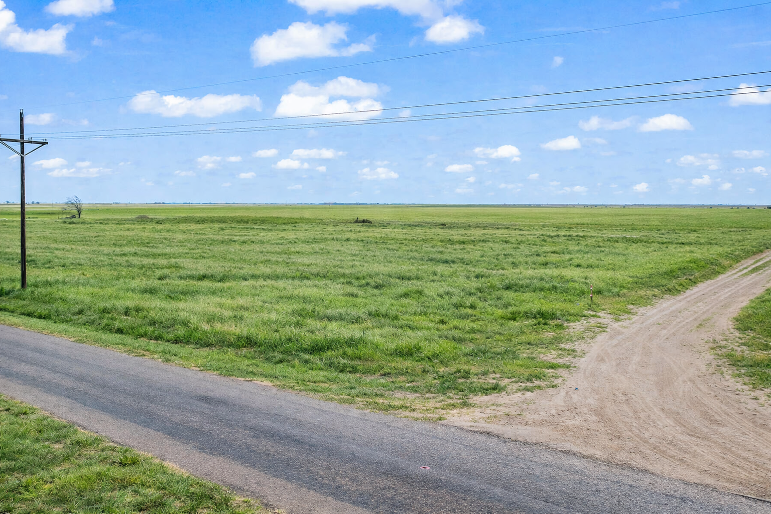 Open grassland beside a paved road with a power line near Idalou, Texas