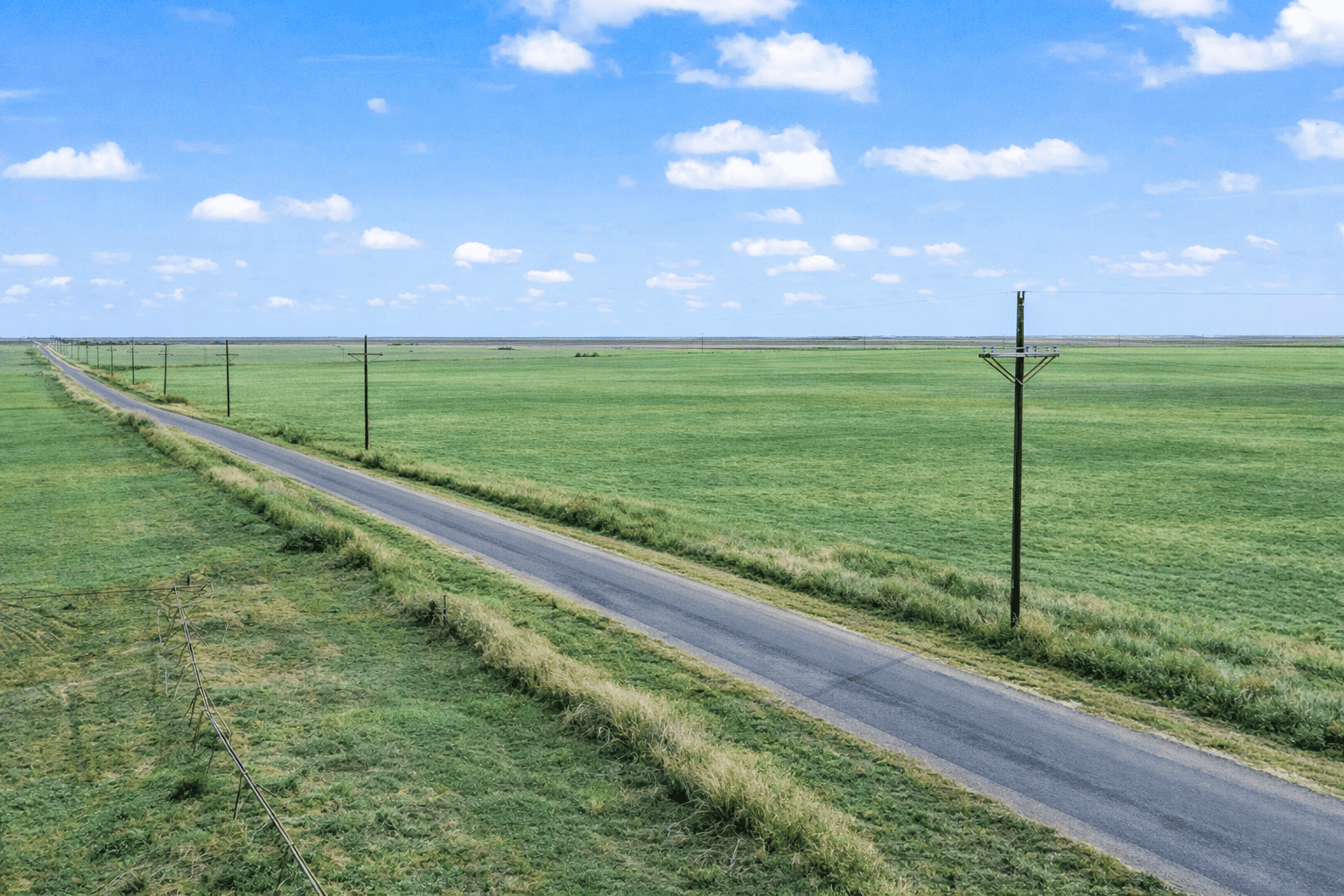 Paved country road with power poles running past open farmland at Reid Farms near Idalou, Texas