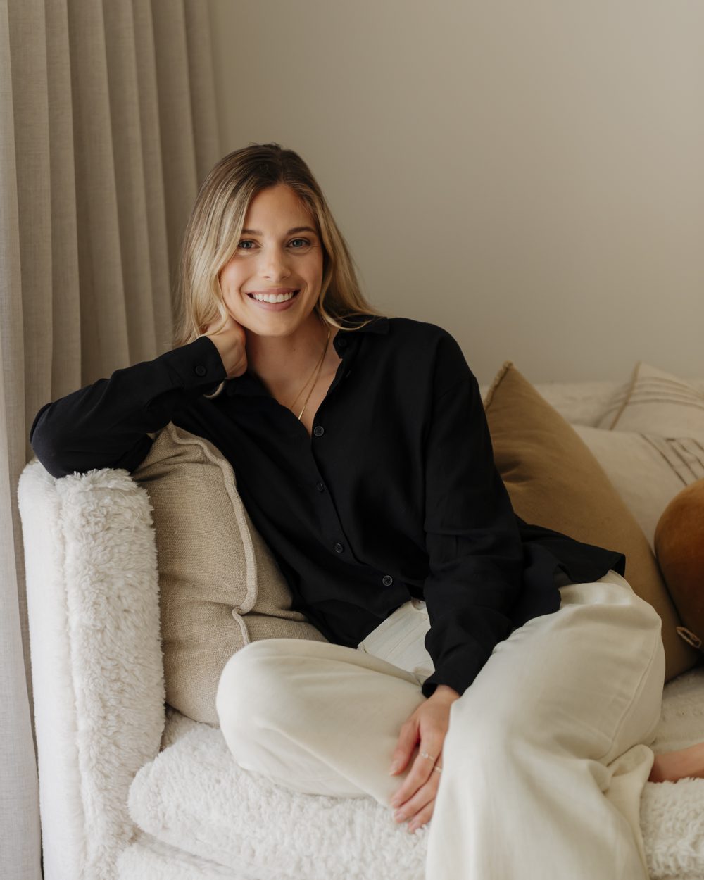 Sydney smiling on a cream couch, in a black shirt