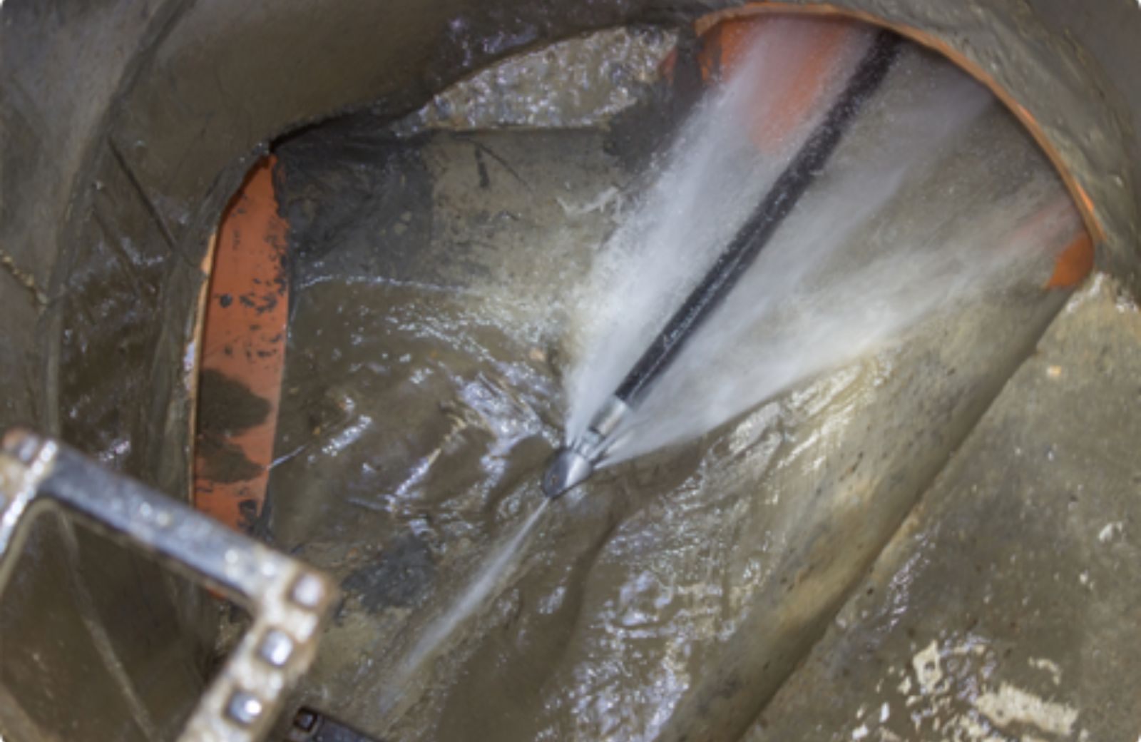 Professional hydro-jetting nozzle spraying high-pressure water to clear a large industrial pipe.