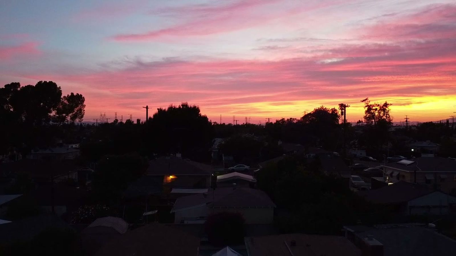 Sunset over a residential neighbourhood, rooftops silhouetted against an orange sky