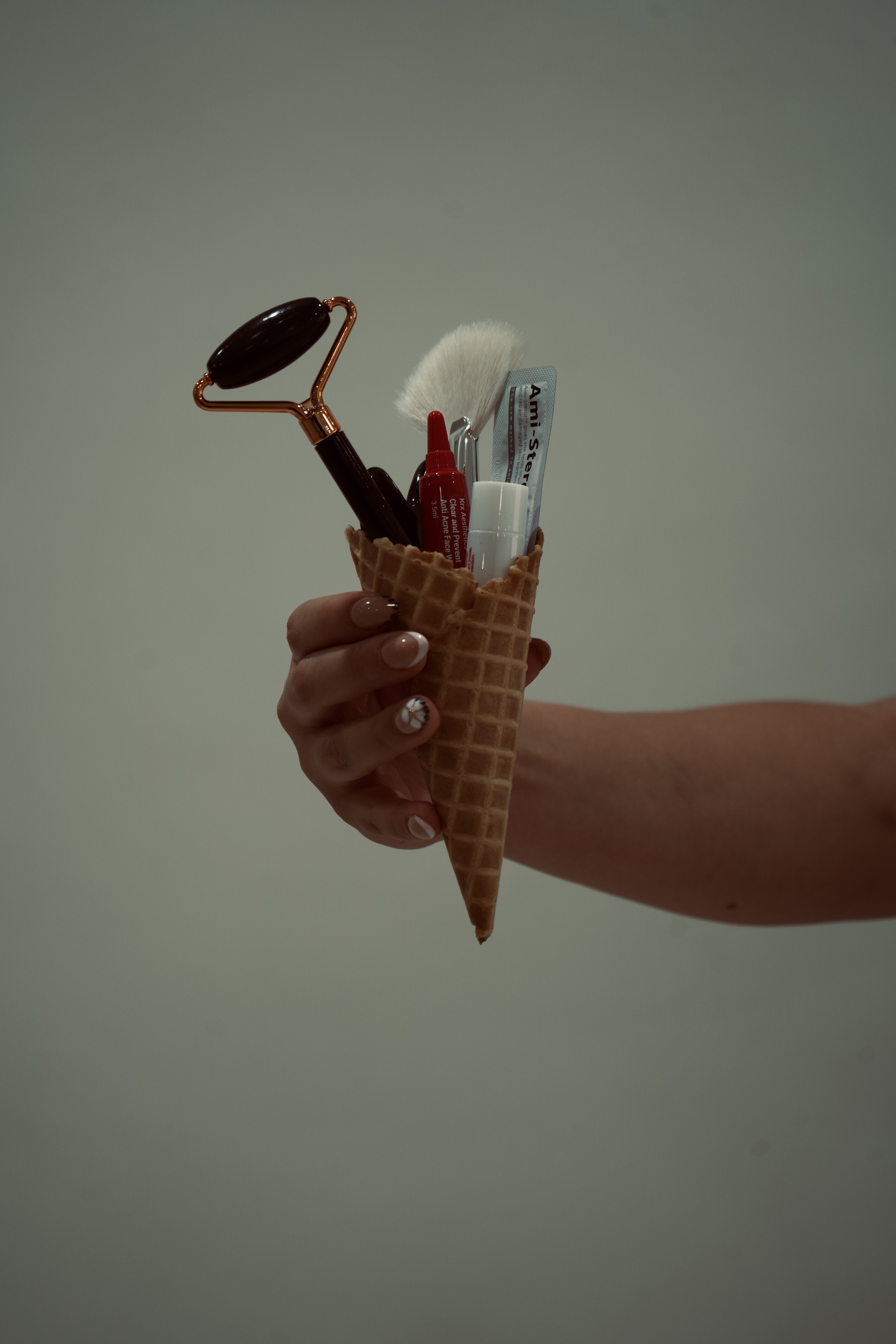 A hand holding skincare products arranged in a waffle cone