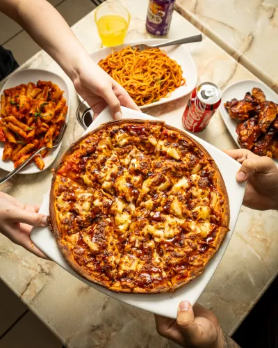 Hands passing a hot pizza across a table full of food
