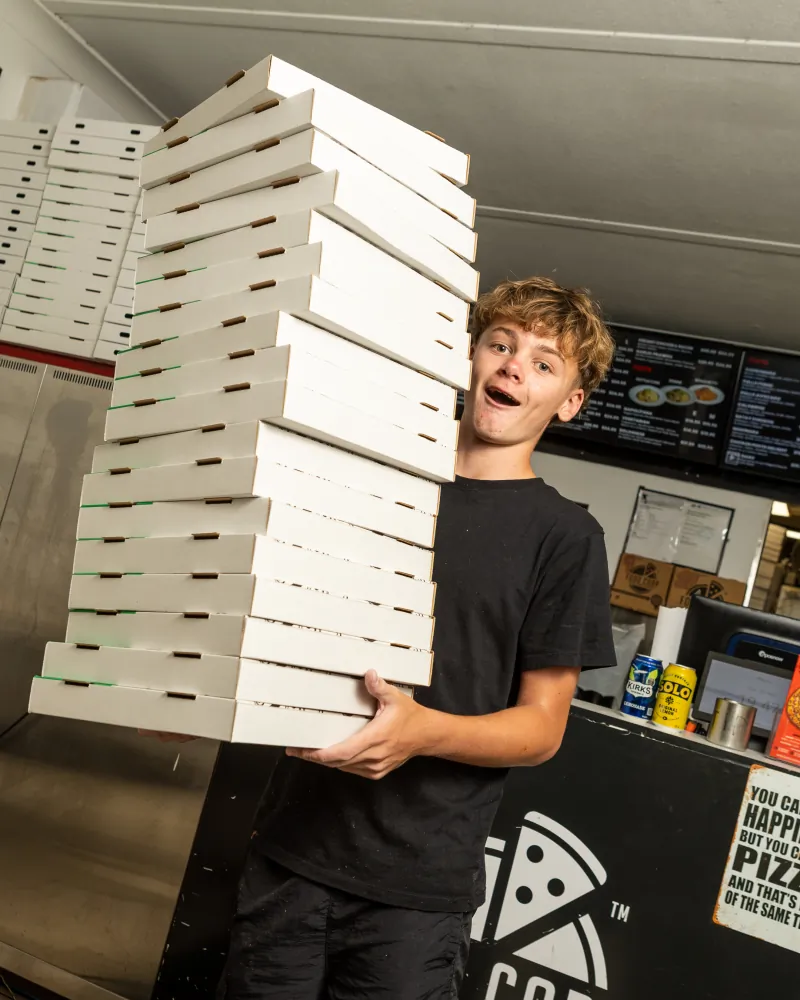 Food Corp Nerang team member carrying a tall stack of pizza boxes for a catering order