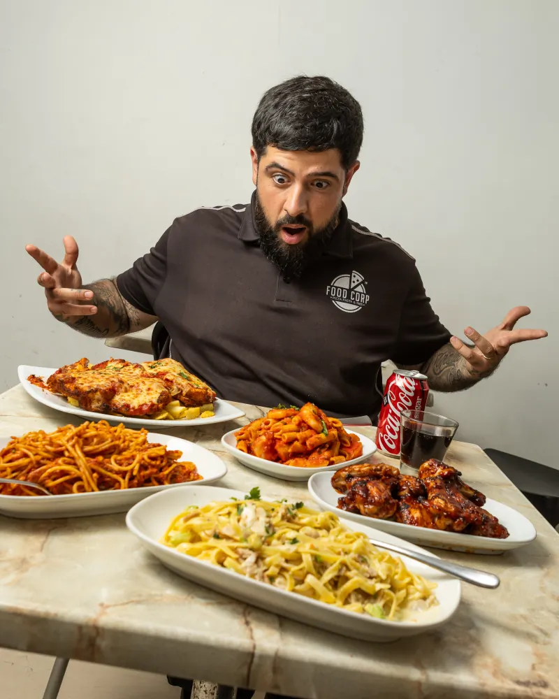 Food Corp owner presenting a table loaded with pizza, pasta, chicken wings and parmigiana