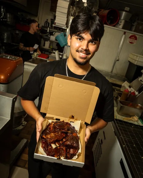 Food Corp staff member holding an open takeaway box of BBQ pork ribs