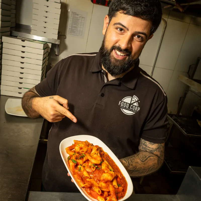 Food Corp owner with a plate of pasta in front of stacked pizza boxes