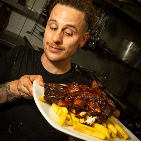 Chef holding a plate of BBQ pork ribs with chips